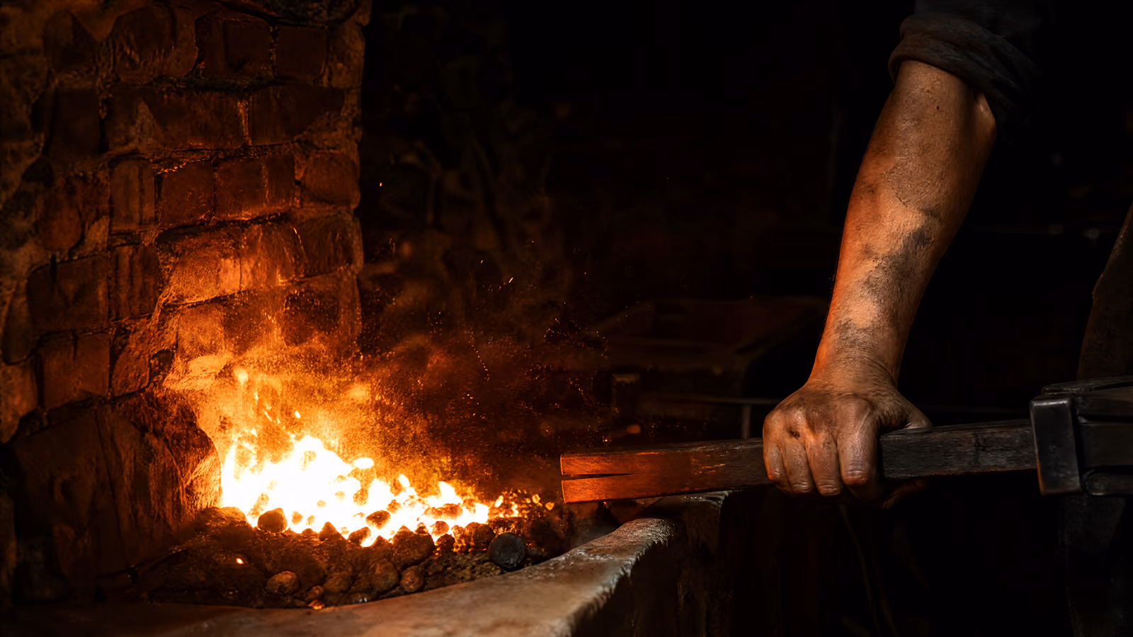 A hand working the bellows beside the hearth, the coals flaring white-orange in response.