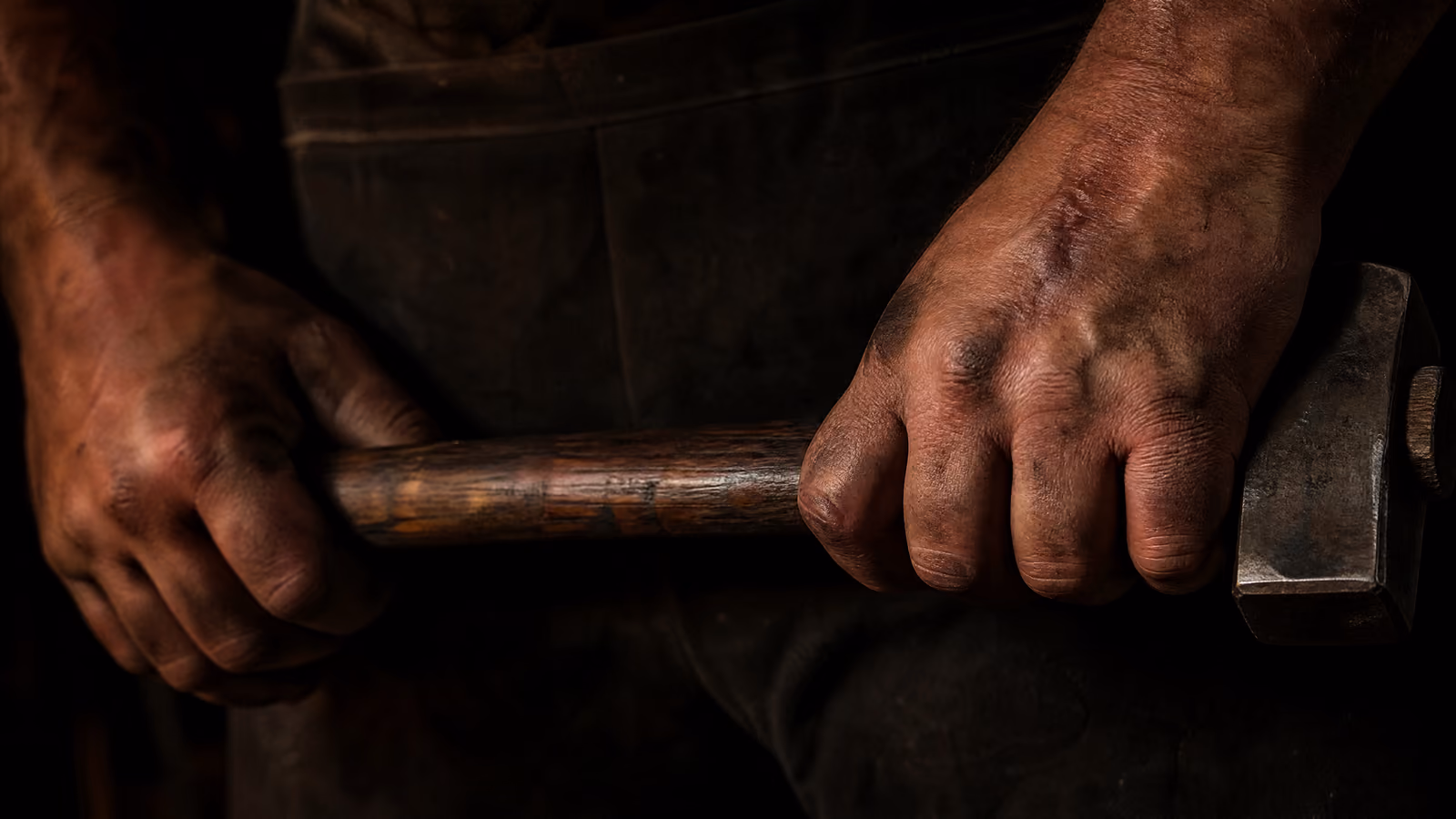 Scarred working hands on a worn hammer haft.