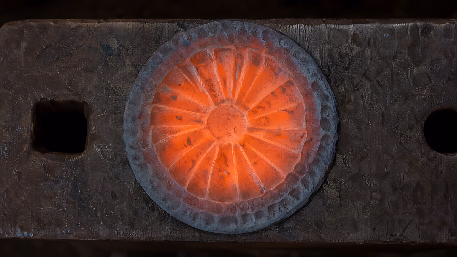 A steel disc on the anvil, still orange at the centre and already grey at the rim.