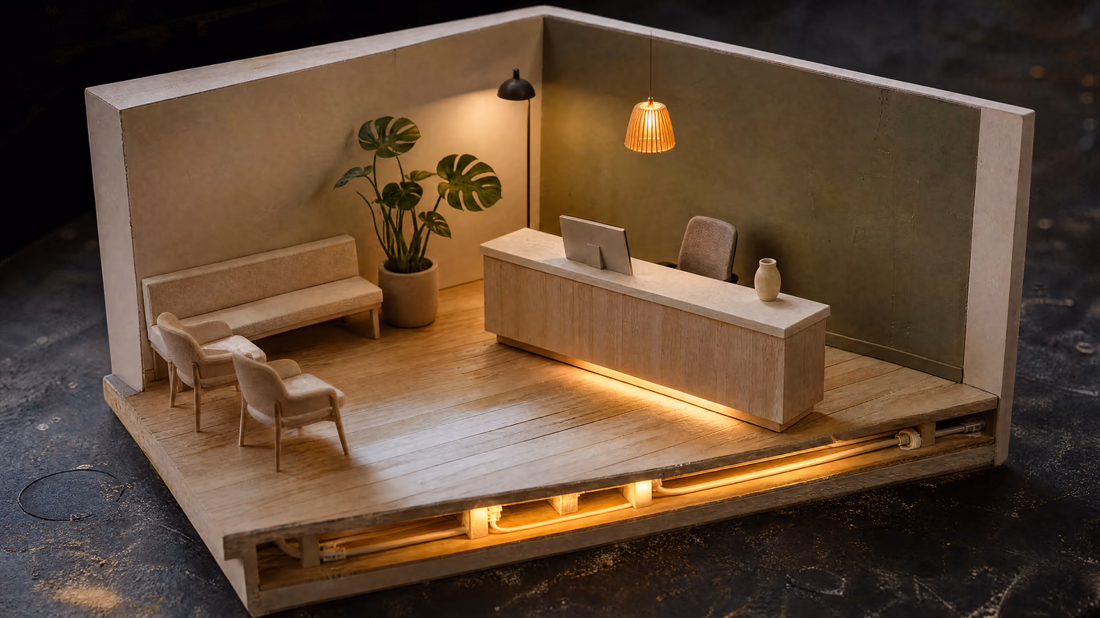 A cutaway model of a modern clinic reception, lit and completely empty: pale oak floors, a low desk with the chair behind it unoccupied, and a line of warm amber light running beneath the floor.