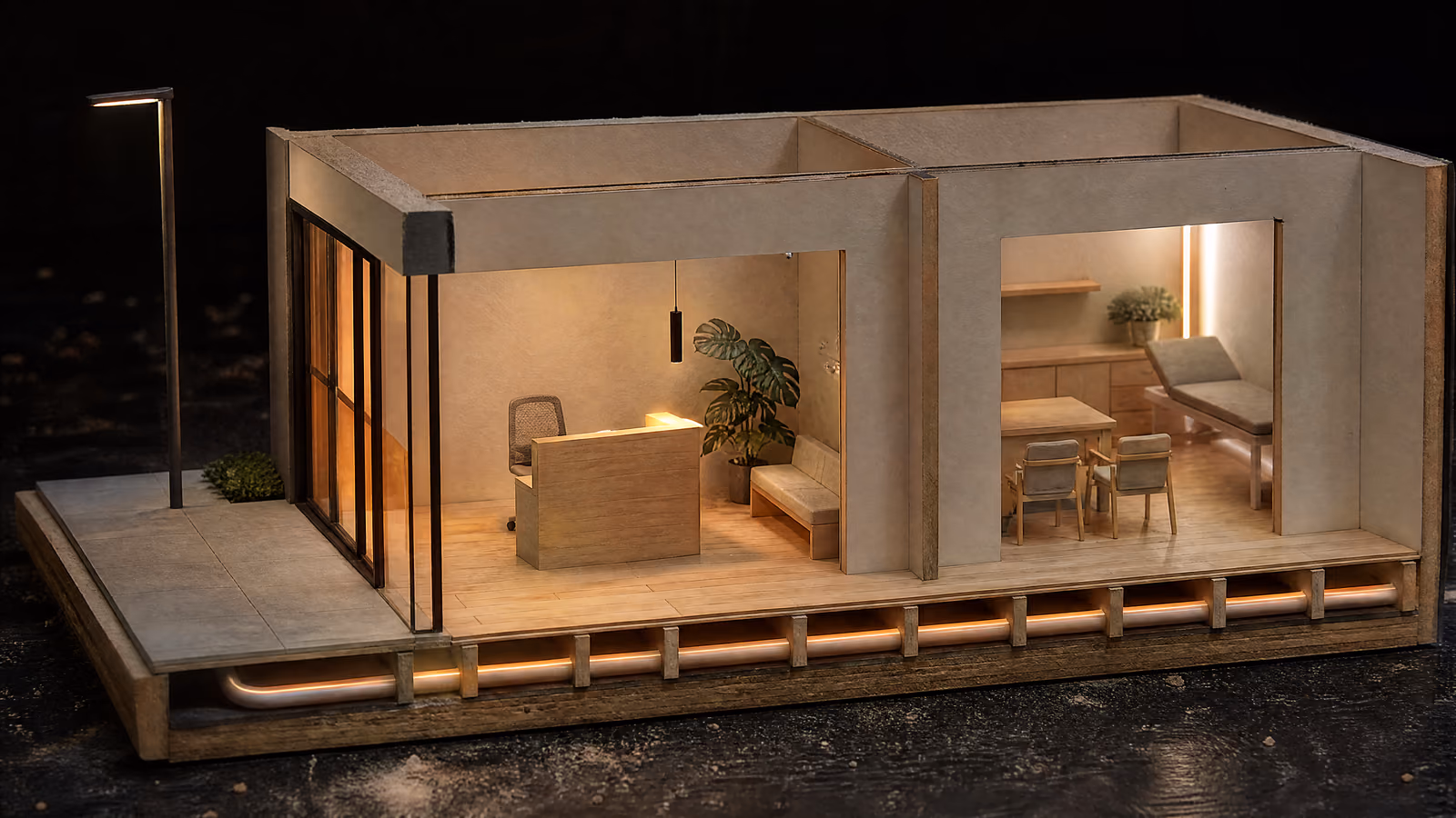 A cutaway model of a modern clinic and the pavement outside it. A glazed entrance on the left, an empty reception in the middle, a consulting room on the right. One continuous line of warm amber light runs beneath all three.